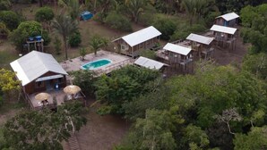 Vista aérea de un resort con varias cabañas de madera, una piscina y exuberante vegetación circundante.