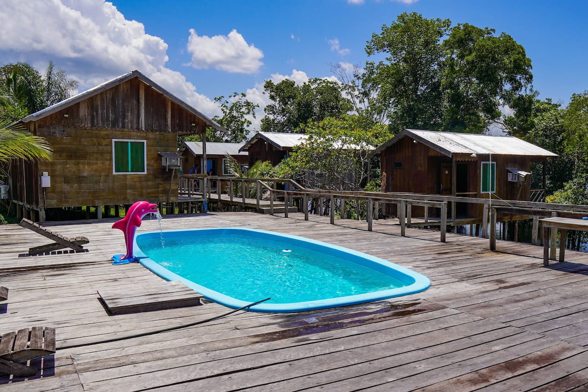 Una terraza de madera con piscina, cabañas de madera y un puesto de socorrista.