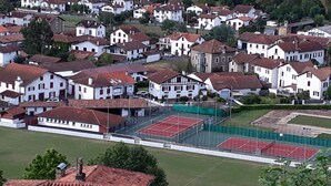 A residential area with houses, a tennis court, and a fenced sports field.