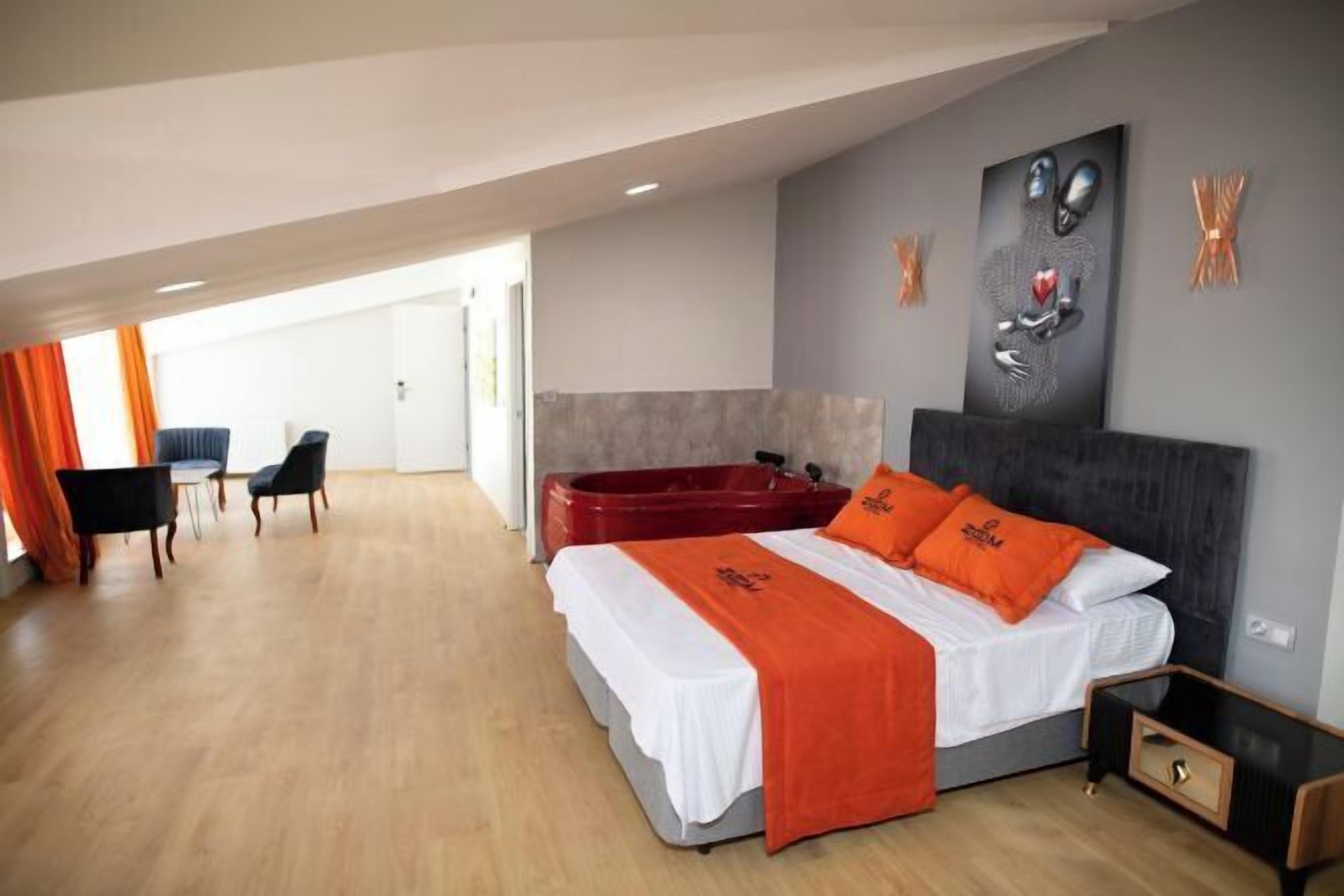 Une chambre d’hôtel moderne équipée d’un lit, d’un jacuzzi rouge, d’un bureau et d’une chaise.