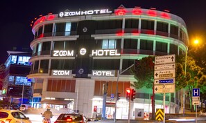 Un hôtel à plusieurs étages, doté d’une enseigne lumineuse sur laquelle on peut lire « Zoom Hotel ».