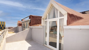 Un edificio residencial con balcón de tejas, un gran ventanal corredero y un toldo marrón sobre las ventanas.