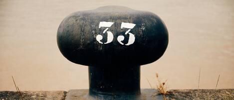 A black bollard with the number 33 painted on it, set in a grassy area with a plain wall in the background.