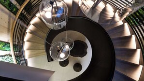 Una escalera de caracol con una columna central, lámparas de cristal y vistas al exterior con vegetación.