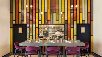 A dining area with a long table, purple chairs, and a colorful striped wall.