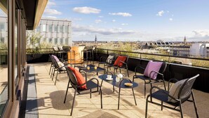 Terraza en la azotea con mobiliario exterior, una mesa con tetera y vistas a la ciudad.