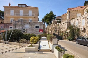 A stone building with a balcony, a sign for a car and scooter rental, and a car parked on the street. - Hedera Estate, Hedera A30 (Dubrovnik)