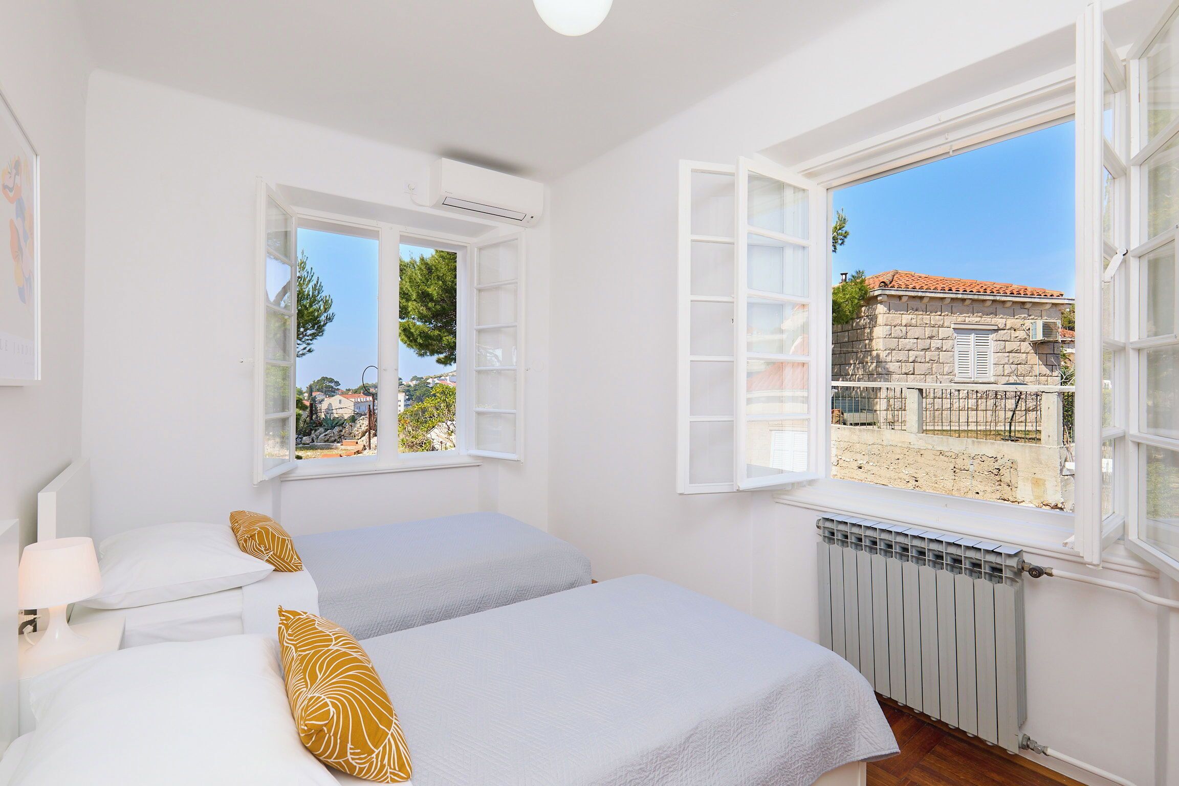 Quarto com duas camas, paredes brancas e uma janela grande com uma persiana aberta.