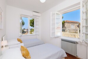 Une chambre avec deux lits, des murs blancs et une grande fenêtre dont le volet est ouvert.
