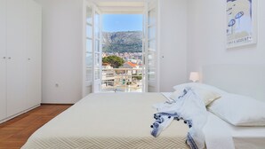 A bedroom with a bed, a wardrobe, and a view of a town and mountains. - Hedera Estate, Hedera A30 (Dubrovnik)