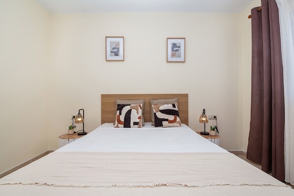 A neatly arranged bedroom with a large bed, two bedside tables with lamps, and two framed pictures on the wall.