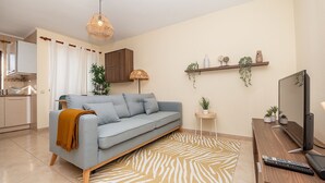 En moderne stue med sofa, fjernsyn og et køkken i baggrunden.