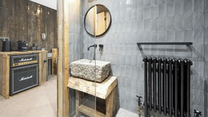 A bathroom with a wooden vanity, a stone sink, a round mirror, and a black radiator. - The Retreat, Windermere (windermere)