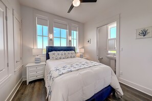 A bedroom with a large bed, two bedside tables, a ceiling fan, and a window with a view. - Luxe seaside home on the golf course with balcony & pool - close to the beach (Port Aransas)