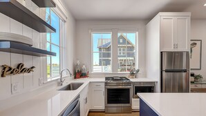Een moderne keuken met witte kasten, roestvrijstalen apparatuur en een groot raam met uitzicht op een woongebouw.