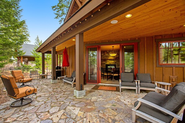 A covered patio with stone flooring, wooden beams, and outdoor furniture.