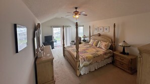 A spacious bedroom with a four-poster bed, a ceiling fan, and a large window offering a view of the outdoors. - On canal. 3 minute walk from beach! 5 minutes from everything!! (Ocean Isle Beach)