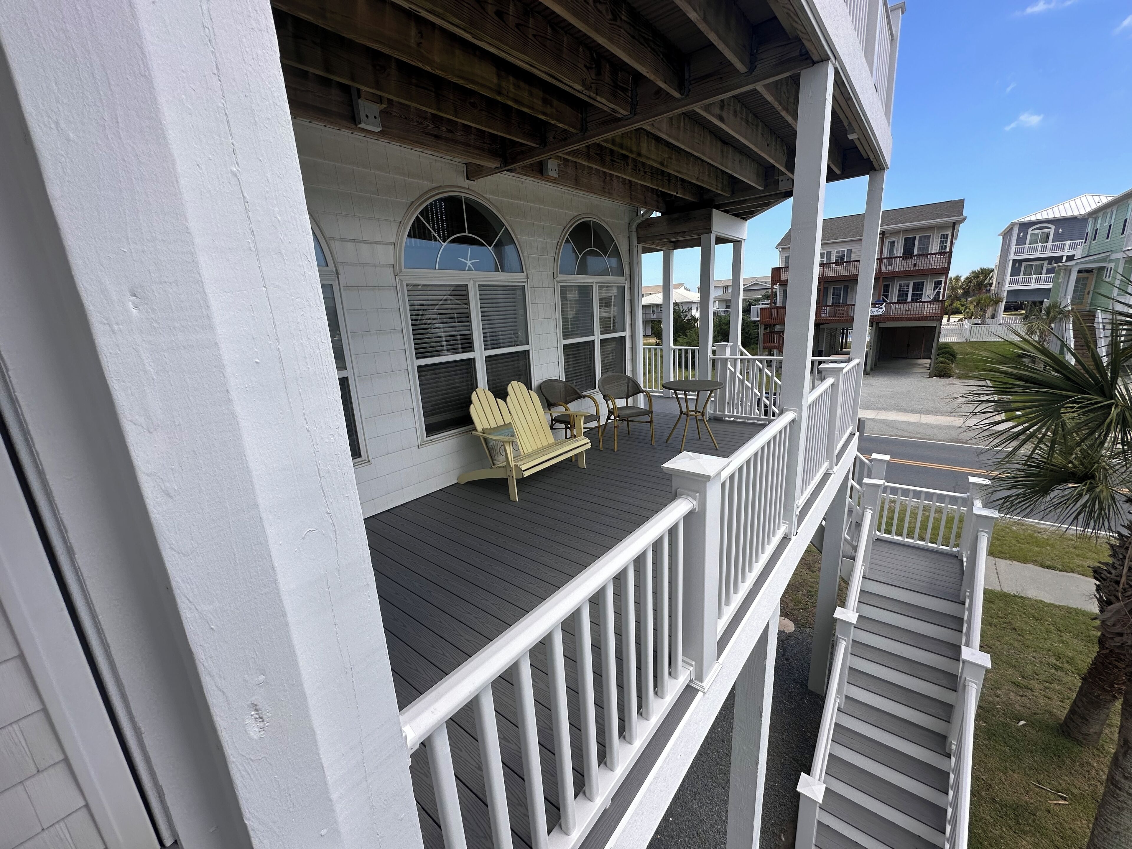 Une terrasse extérieure couverte, dotée de chaises Adirondack et d’une petite table, qui offre une vue sur une rue bordée d’autres immeubles.