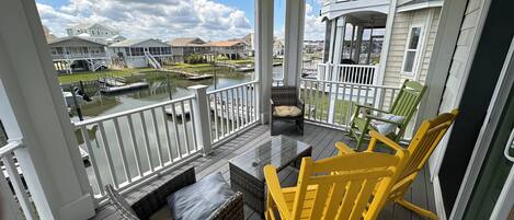 A covered balcony with wicker furniture and a view of a marina.