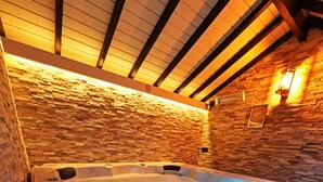 A hot tub with a stone wall backdrop and wooden beams. - Potter's Place by Ardenne Places (Spa)