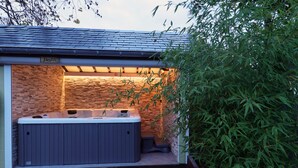 A hot tub in a covered outdoor area with a brick wall and bamboo plants. - Potter's Place by Ardenne Places (Spa)