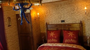 A room with a bed featuring 'Harry Potter' themed bedding, a blue plush toy, a chandelier, and a wall with a map design. - Potter's Place by Ardenne Places (Spa)