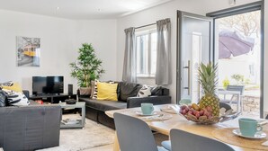 En moderne stue med sofa, fjernsyn og spiseområde med et bord dækket til to.