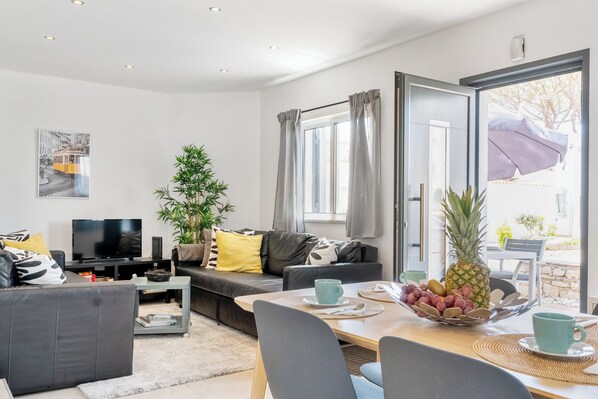 A modern living room with a sofa, TV, and dining area with a table set for two.