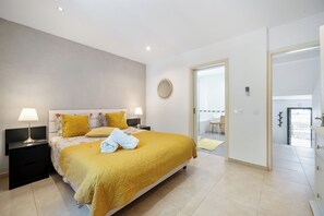 A modern bedroom with a large bed, bedside lamps, and a view to a balcony.