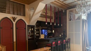 Un área de bar con una barra, taburetes y una pantalla de televisión. Se observan puertas rojas y una araña.
