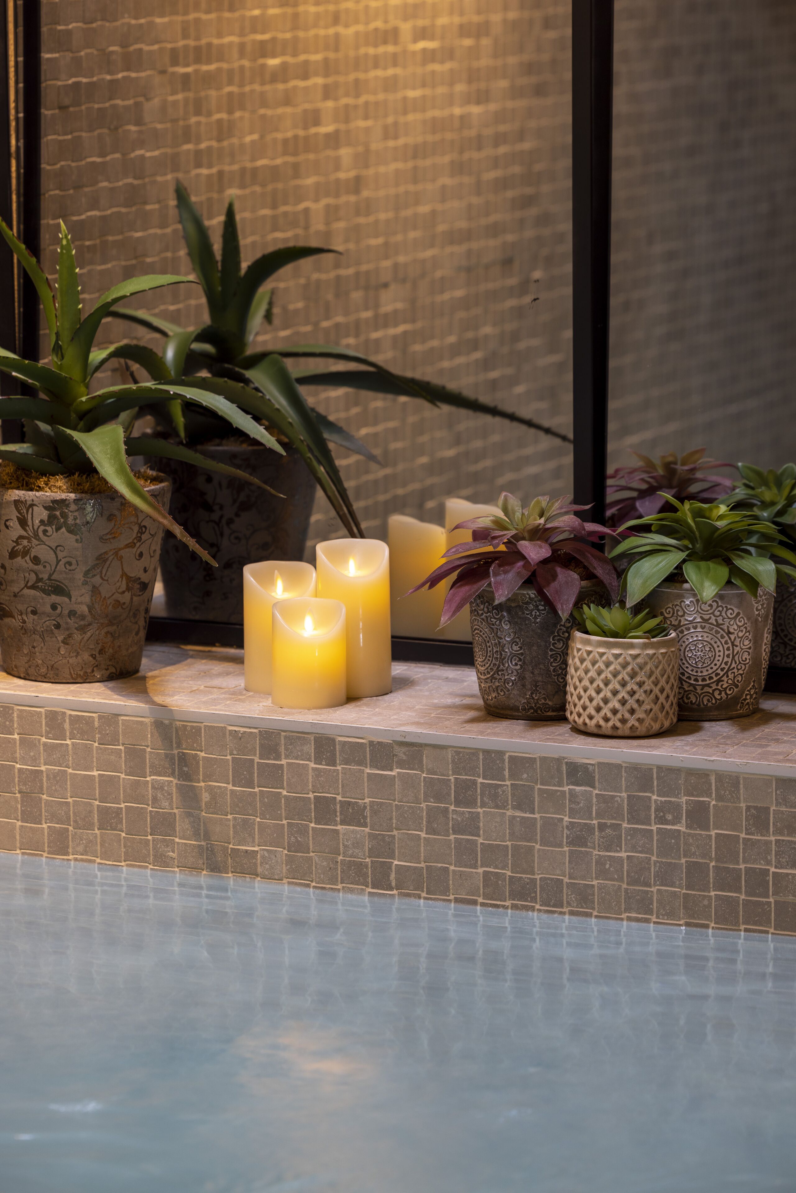 A tiled ledge with potted plants and candles.