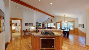 A spacious kitchen with a central island, wooden flooring, and a dining area with a large window. - Split Rock Hideaway with Access to Exclusive Golf (Sunriver)