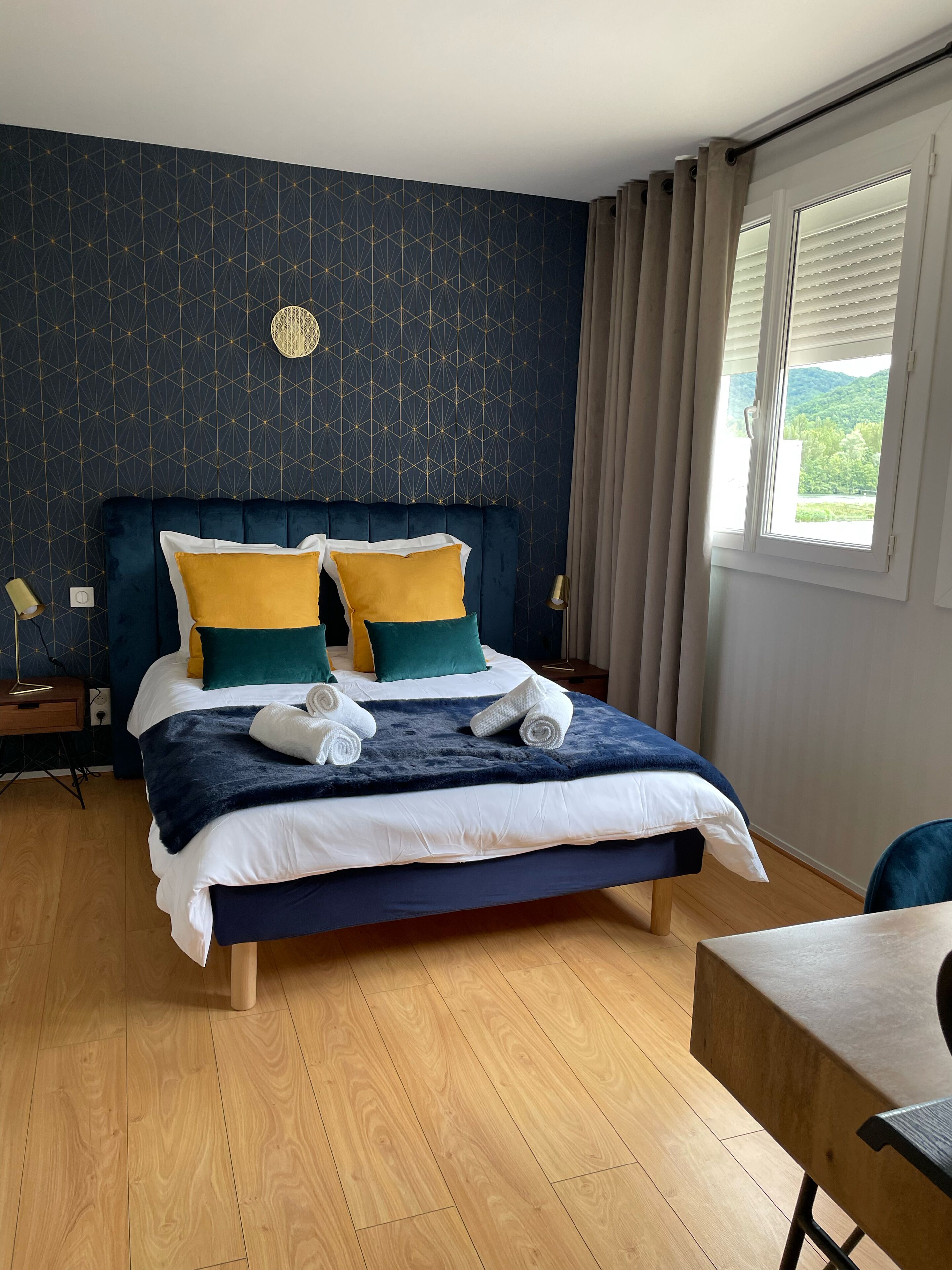 A neatly made bed with a dark blue headboard, white and yellow pillows, and a blue blanket.