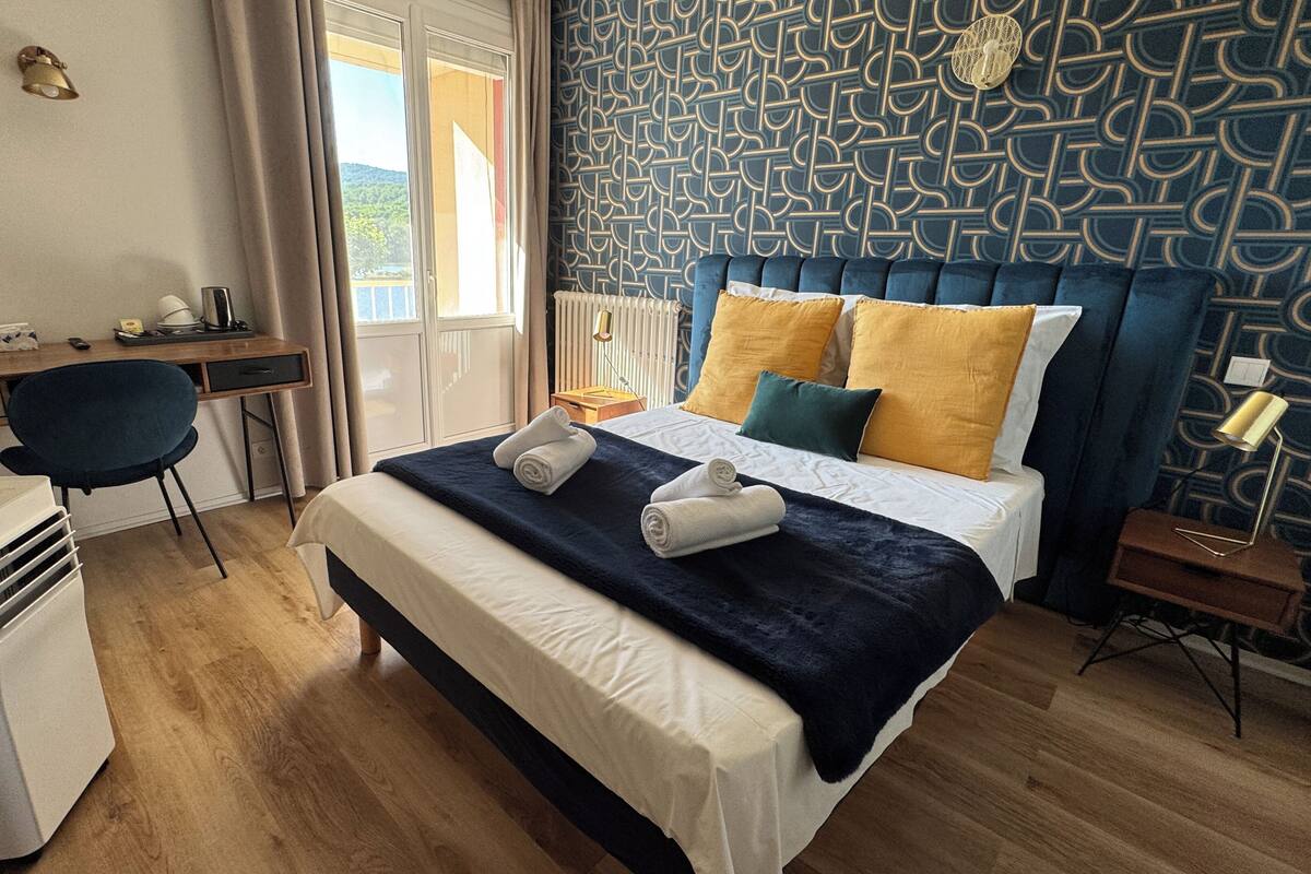 Hotellihuone, jossa on sänky, työpöytä, tuoli, lämmitin ja ikkuna, jossa on verhot.