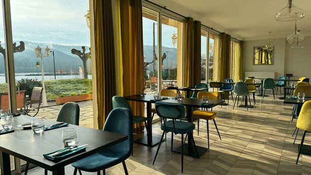 A restaurant with tables and chairs, large windows, and a view of the outdoors. - Hôtel Restaurant du Lac (Boussens)