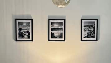Uma sala de estar moderna com um sofá azul, uma poltrona mostarda, uma mesa de centro redonda e um lustre. Três fotografias emolduradas estão expostas na parede.