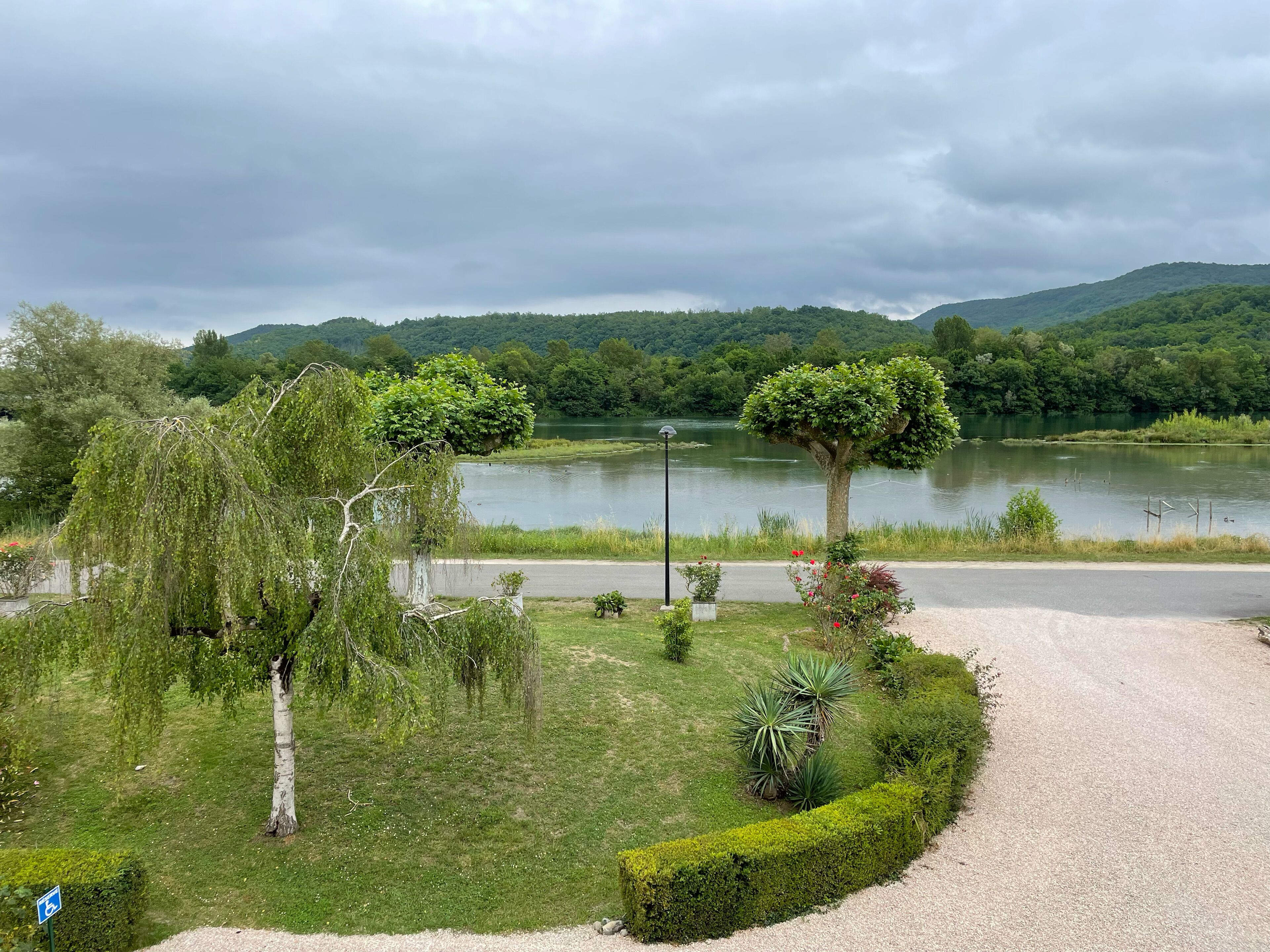 Un parque con un lago, árboles y un camino de grava.