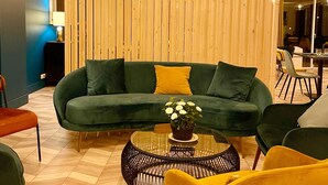 A modern living room with a green sofa, yellow chairs, and a round coffee table with a flower centerpiece. - Hôtel Restaurant du Lac (Boussens)