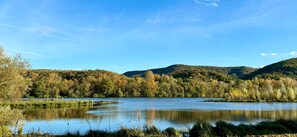 A calm lake surrounded by forested hills under a clear sky. - Hôtel Restaurant du Lac (Boussens)