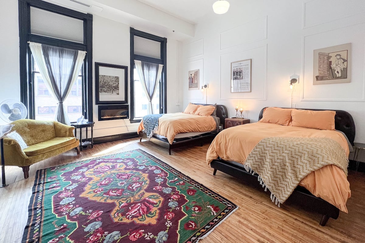 A hotel room with two beds, a sofa, a large patterned rug, and artwork on the walls.