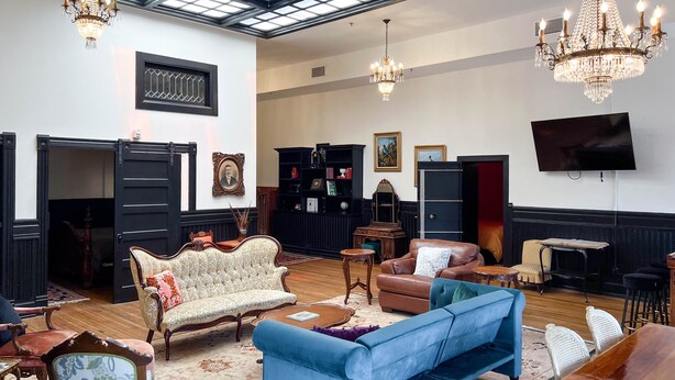 A spacious room with a high ceiling, chandeliers, a large window, and a television. - The Oliver Inn | Duluth Hotel Near Canal Park (Duluth)