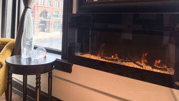 A room with a fireplace, a window with a view of a street, and a small table with a cat figurine.