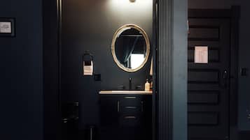 Um banheiro com decoração escura, um espelho redondo, uma pia e uma toalha pendurada na parede.