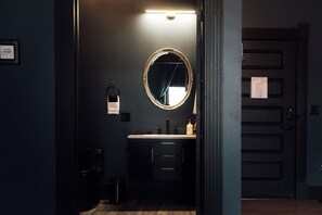 A dark-themed bathroom with a round mirror, a sink, and a towel hanging on the wall.