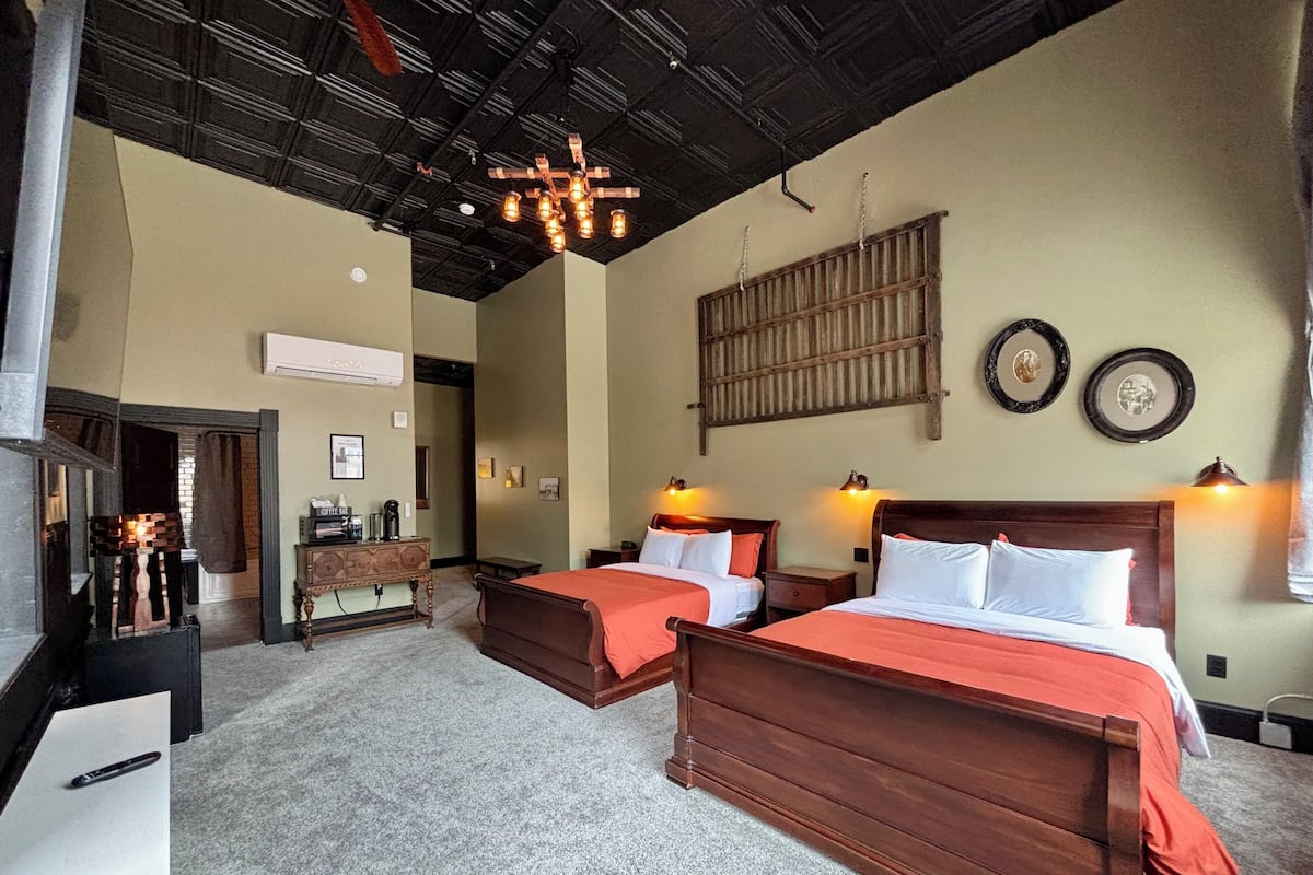 A hotel room with two wooden beds, a large wooden headboard, a fireplace, and a ceiling with exposed beams.