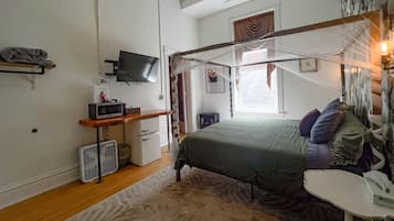 A bedroom with a bed, a desk, a television, a small heater, and a window with curtains.