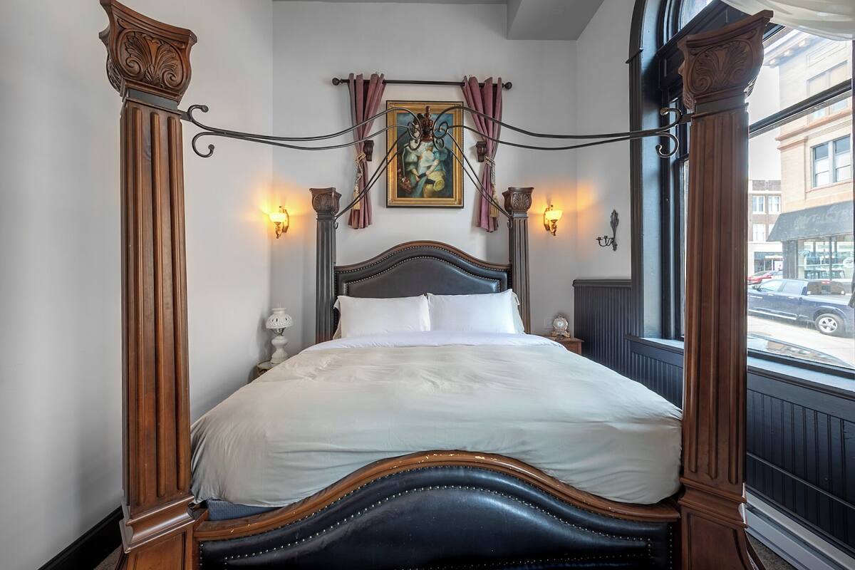 A four-poster bed with a dark headboard, white linens, and wall sconces.