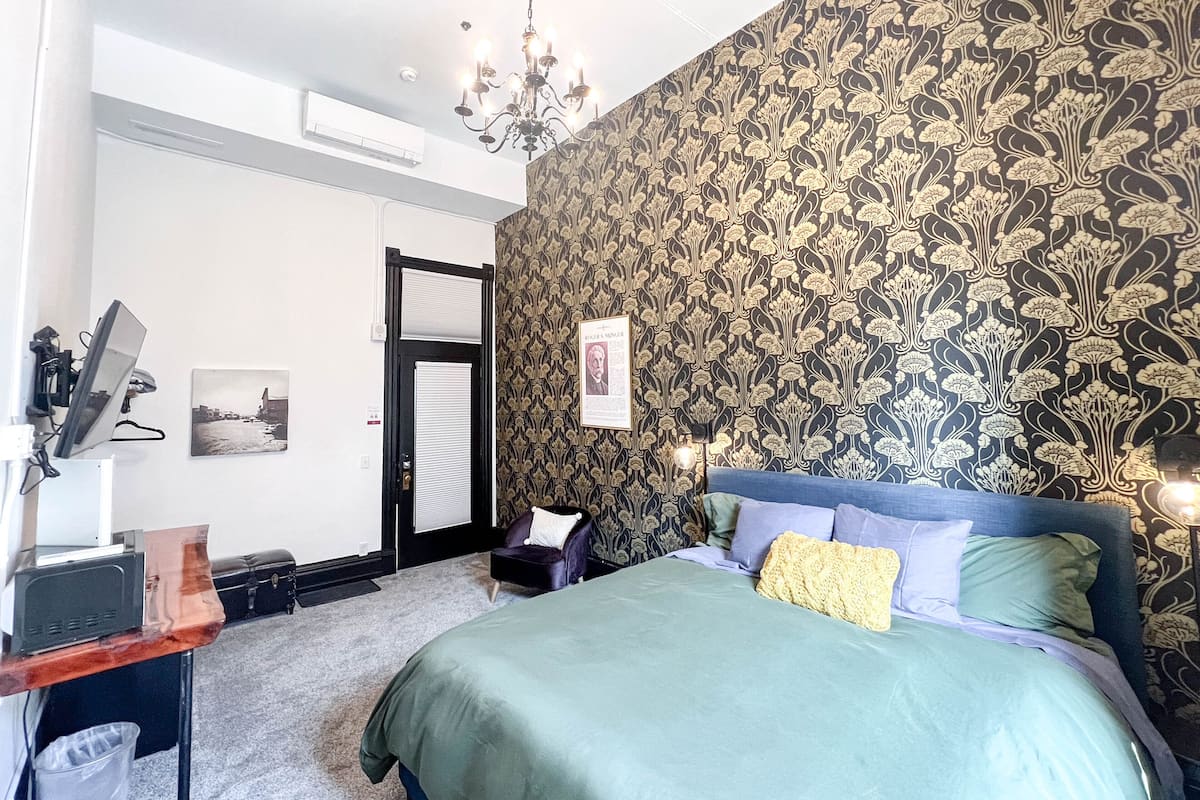 A bedroom with a bed, a desk, a chair, a chandelier, and a door.