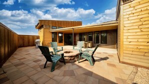 A modern outdoor patio with Adirondack chairs, a fire pit, and a wooden deck.