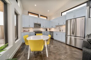 A modern kitchen with light blue cabinets, stainless steel appliances, and a round table with yellow chairs.